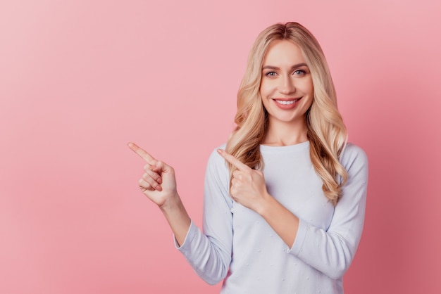 Portrait of positive cheerful pretty lady direct finger empty space on pink background