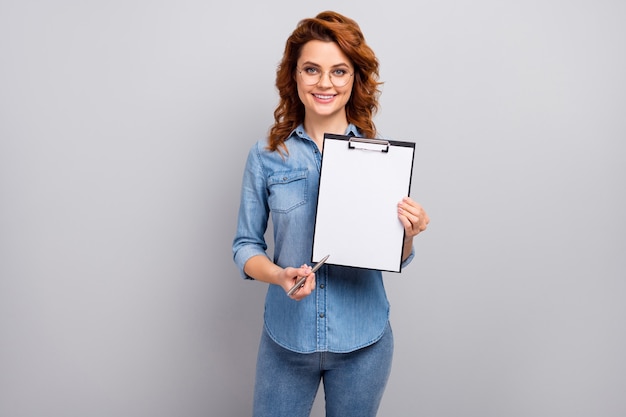 Portrait of positive cheerful smart manager woman hold paper clipboard point empty space pen for clients sign contract wear style trendy clothes isolated over grey color wall