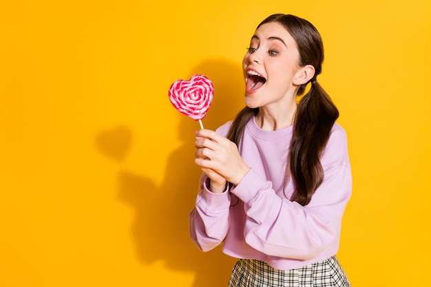 Portrait of positive cheerful teen girl try bite heart shape candy