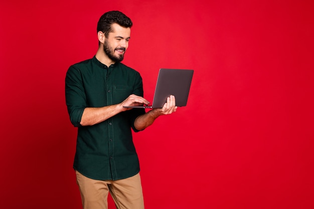 Портрет позитивного жизнерадостного работника, стоящего на copyspace с использованием своего ноутбука, имеющего рабочую мастерскую с коллегами в повседневных коричневых брюках
