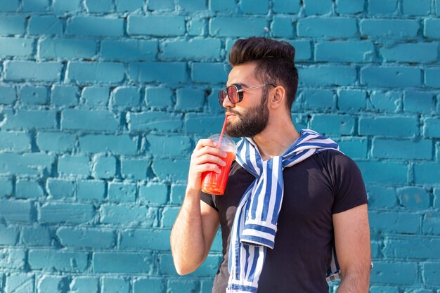 Portrait of a positive cheerful young arab man with a glass of juice with a straw while walking in