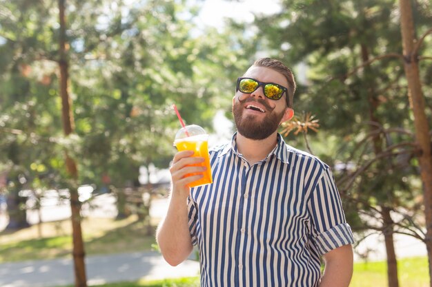 歩きながらストローでジュースのガラスと前向きな陽気な若い男の肖像画