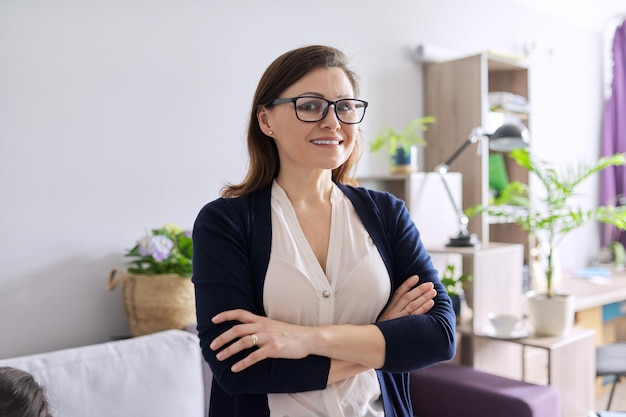 Portrait of positive confident middle aged woman with arms crossed, female teacher, counselor, tutor, coach working in office, smiling looking at camera