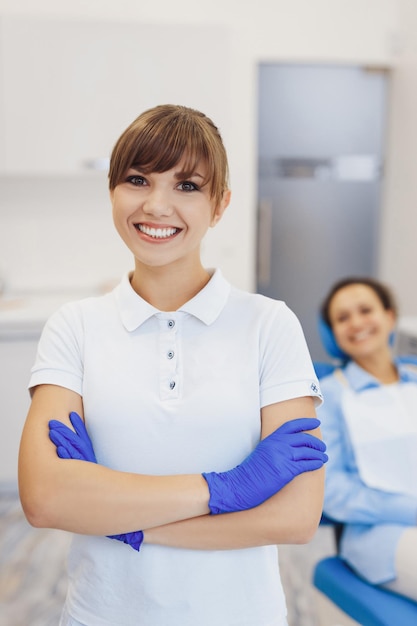 Portrait of positive dental doctor smiling at camera in dentistry room Female doctor with crossed hands wearing latex gloves