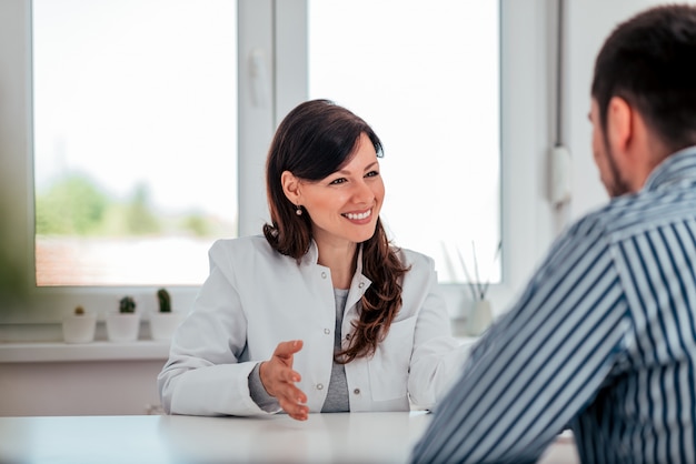 Portrait of a positive female doctor talking to a male patient in medical office.