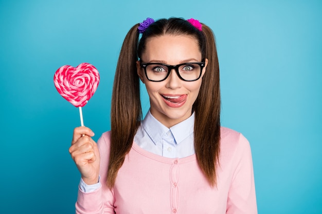 portrait of positive funky girl high school student hold heart shape lollipop want eat lick lips