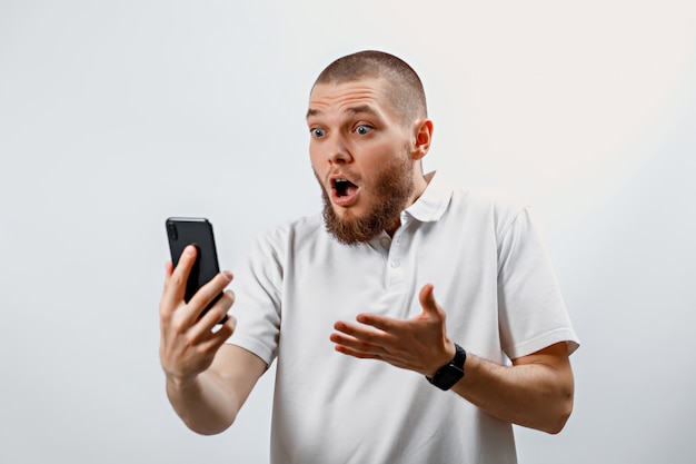 Portrait of a positive handsome bearded man in a white t-shirt talking on video call using a smartphone