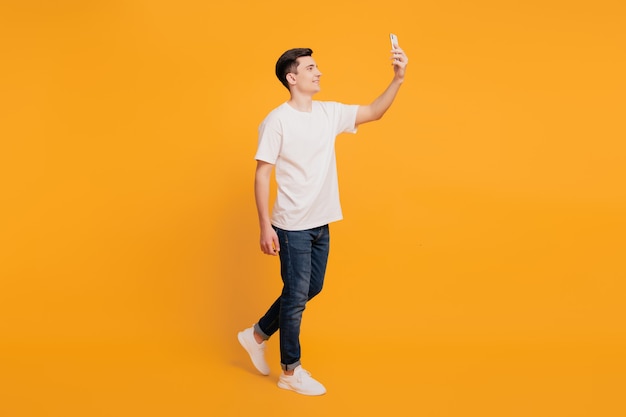 Portrait of positive handsome guy take selfie hold phone walk on yellow background