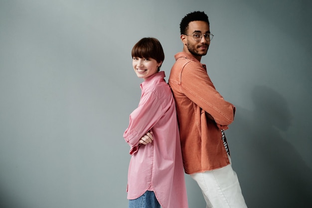 Portrait of positive interracial couple of models standing back to back and crossing arms on chest a