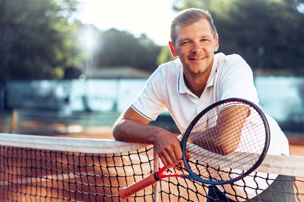 Портрет позитивного мужского теннисиста с ракеткой, стоящего на грунтовом корте