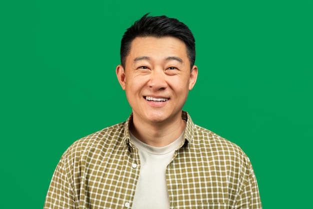 Portrait of positive mature asian man looking and smiling at camera posing over green background