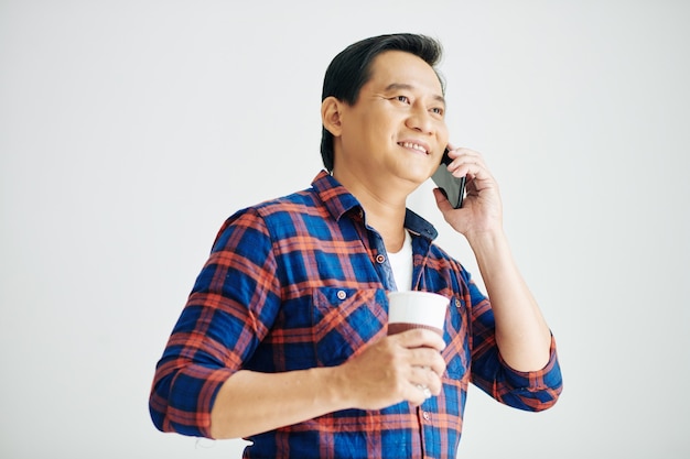 Portrait of positive mature man drinking take out coffee and calling on phone