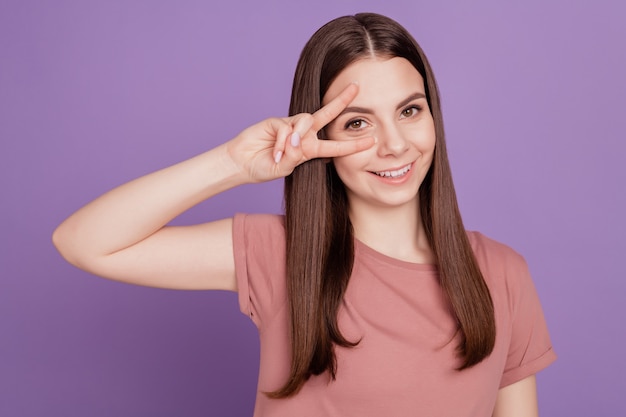 Il ritratto di una bella ragazza positiva si diverte a gesticolare due v-segni isolati su sfondo viola