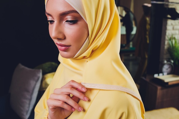 ピンクのスカーフをかぶったポジティブなかなり若いアラビア人女性が手で顔に触れる肖像画