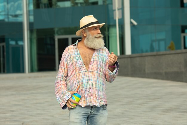 Ritratto di uomo positivo senior barbuto hipster, avendo pausa caffè all'aperto su contesti urbani.