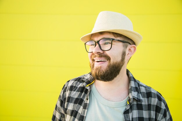 Портрет позитивного молодого хипстера, улыбающегося над желтой стеной магазина на открытом воздухе, красивый т