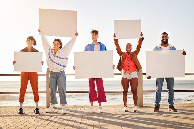 Foto poster ritratto e diversità con gli amici insieme che tengono segnaletica in segno di protesta sulla passeggiata in riva al mare mockup di libertà e cartellone pubblicitario con un gruppo di amici uomo e donna che tiene cartelli vuoti