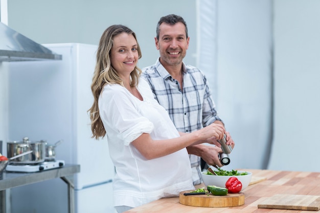 Portrait of pregnant couple preparing salad in kitchen