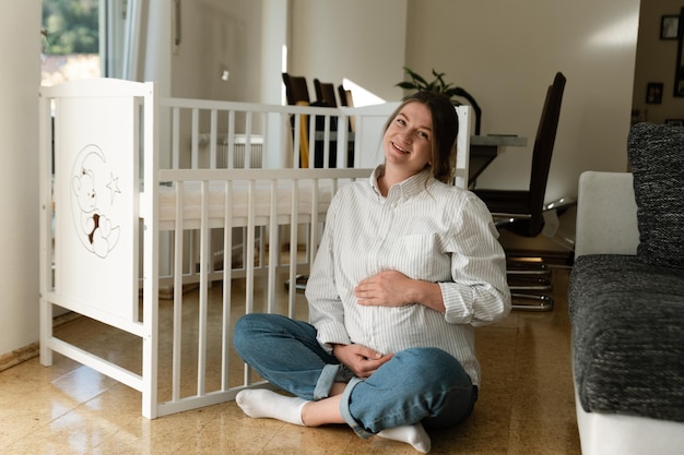 Photo portrait of a pregnant girl sitting near the crib pregnant woman at home