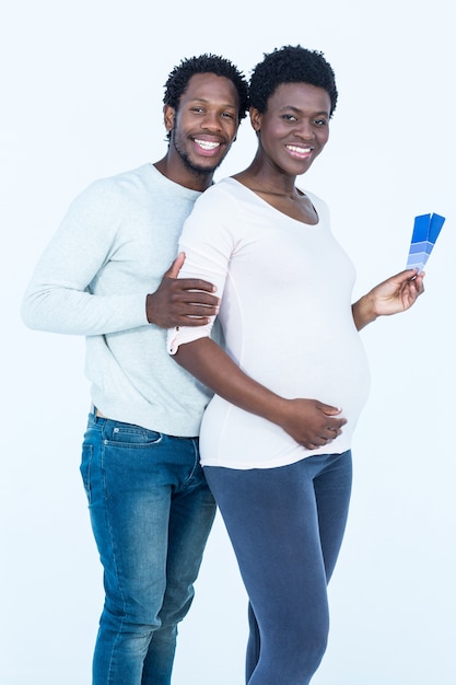 Portrait of pregnant wife holding color swatches while standing with husband 