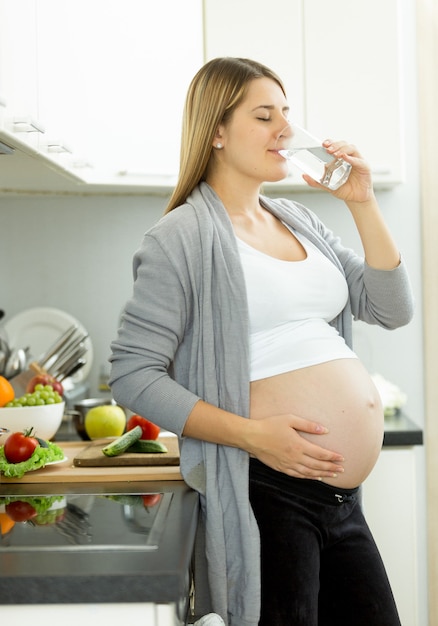 Portrait of pregnant woman drinking water on kitchen