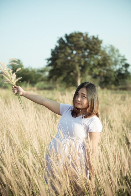 フィールド上の妊婦の肖像画アジアの女性は日没時に草の花を保持します