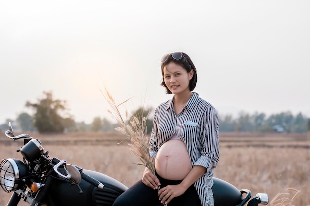 Portrait of pregnant woman sitting with plants on motorcycle in farm against sky