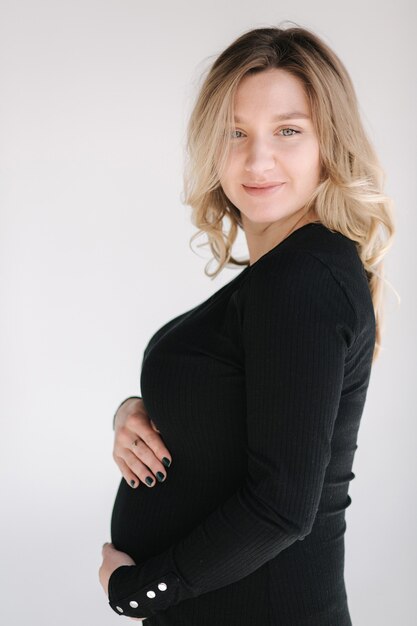 Portrait of pregnant woman in studio on white background beautiful future mother put her her hands