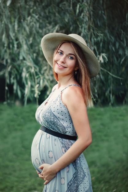 Portrait of pregnant woman touching abdomen while standing on grass