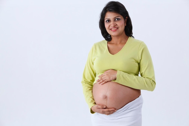 Photo portrait of pregnant woman touching belly while standing against white background