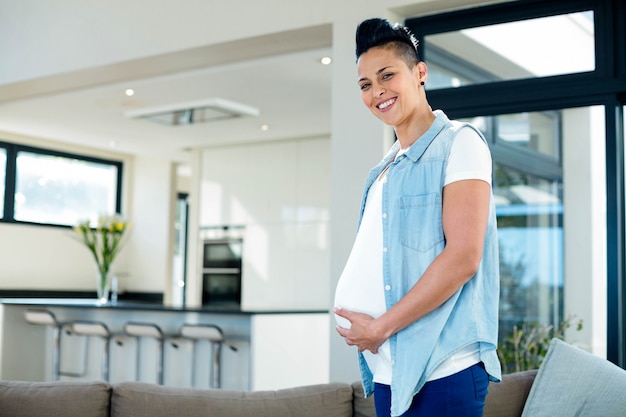 Portrait of pregnant woman touching her belly in living room