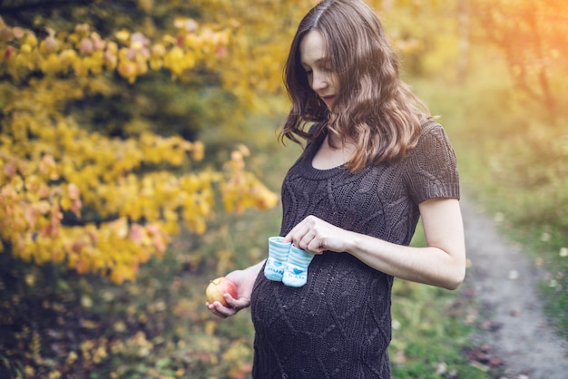 Portrait of pregnant woman with booties on her tummy in the autumn forest