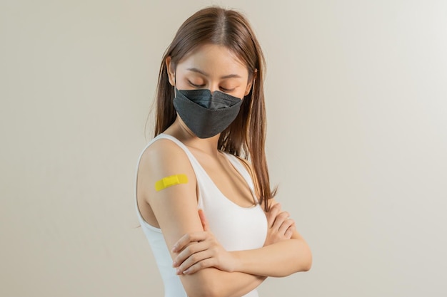 Portrait of pretty beautiful asian young teenage attractive after getting receive anti virus vaccine covid19 Showing arm on yellow bandage isolated on white background copy space