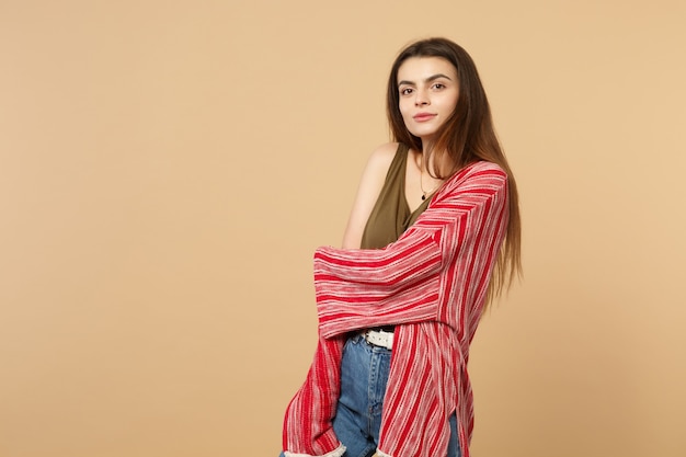 Portrait of pretty beautiful young woman in casual clothes standing, looking camera isolated on pastel beige wall background in studio. People sincere emotions, lifestyle concept. Mock up copy space.