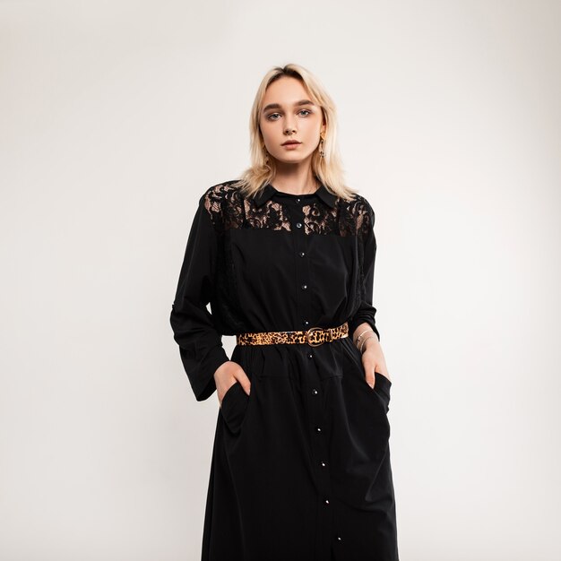 portrait pretty beautiful young woman in elegant black dress with leopard strap near vintage white wall indoors.