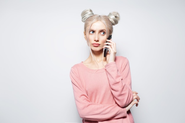Portrait of pretty blonde girl with hair buns talking on smartphone on white