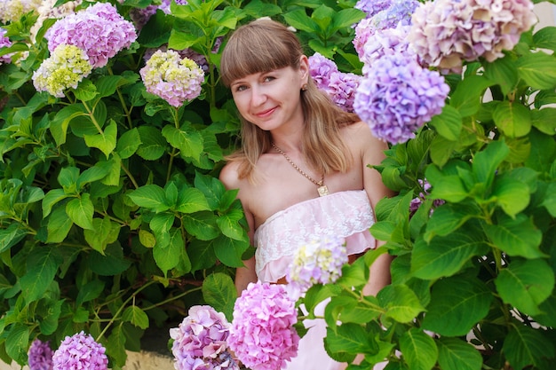 Ritratto della bionda graziosa all'aperto con l'ortensia rosa lilla. bella donna nel parco fiorito di primavera in una giornata di sole. donna felice che gode di una passeggiata nella natura.