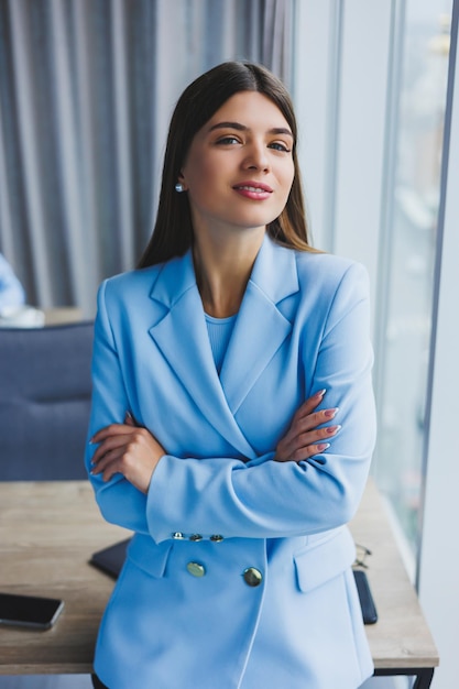 Portrait of a pretty brunette in a blue jacket in the office near the panoramic window with a view of the city Happy business woman in the office