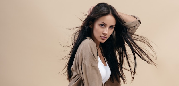 Portrait of pretty brunette girl with healthy long hair on beige