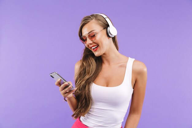 夏服とサングラスワイヤレスヘッドフォンとスマートフォンを使用して音楽を聴くのかなりブルネットの女性の肖像画