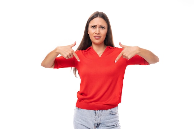 portrait of a pretty brunette woman with straight hair in a red tshirt and jeans pointing with her hands at the advertising space