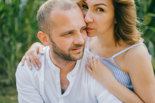 Portrait of pretty caucasian woman with short dark hair in blue dress with her strong husband relaxes together in the village cornfield.