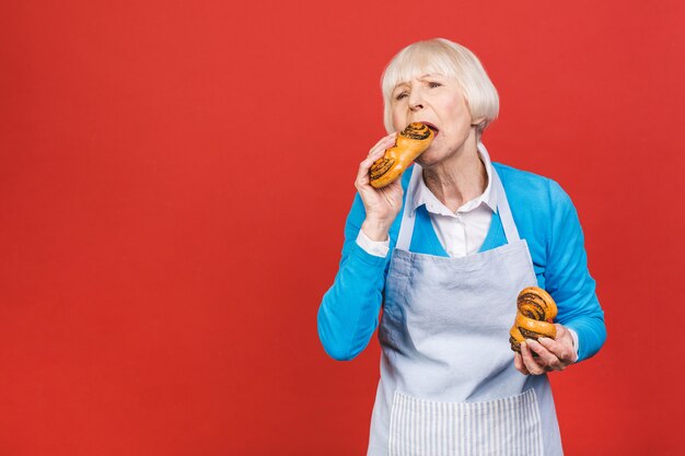 Ritratto della donna invecchiata senior allegra abbastanza affascinante con la grinza che mostra gesturing forno casalingo dolce