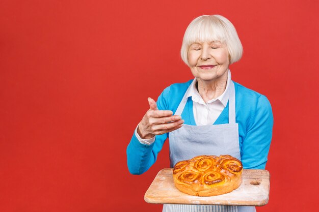 Ritratto della donna invecchiata senior allegra abbastanza affascinante con la grinza che mostra gesturing torta casalinga dolce