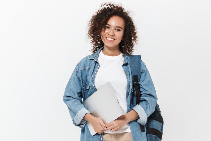 Photo portrait of a pretty cheerful casual african girl carrying backpack standing isolated over white wall, holding laptop computer