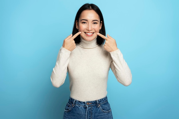 Portrait of pretty cheerful woman points index fingers at smile shows white teeth