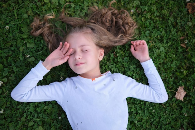 Portrait of pretty child girl outdoors lying down on grass lawn