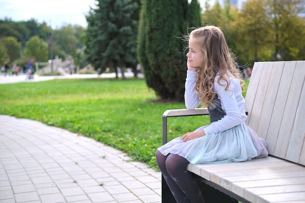 Portrait of pretty child girl sitting on park bench outdoors