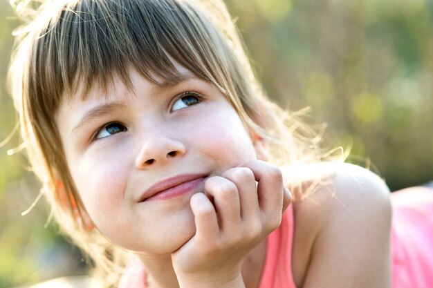 灰色の目と彼女の手に寄りかかって屋外で幸せに笑っている長い金髪のかわいい子供の女の子の肖像画