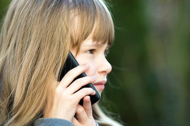 Foto ritratto della ragazza graziosa del bambino con capelli lunghi che comunicano sul telefono cellulare